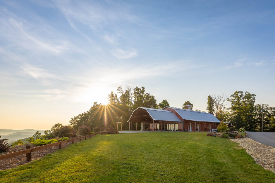 Hidden Hill Venue on the hill at sunset. Red building with metal roof surrounding by lush green lawn.