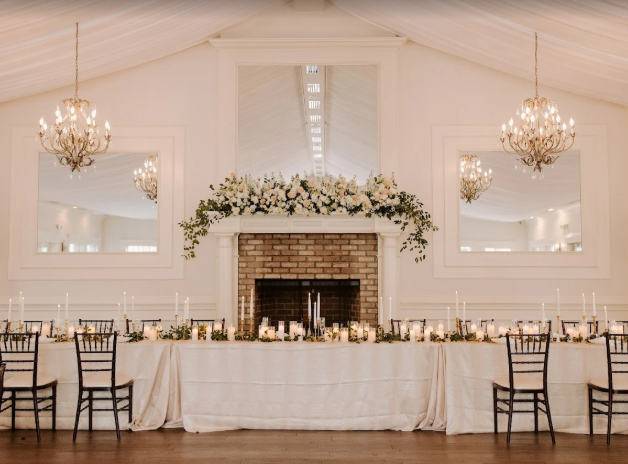 Reception area in Highgrove Estates with a large brick fireplace and mirrors and long tables with linens, candles and florals.