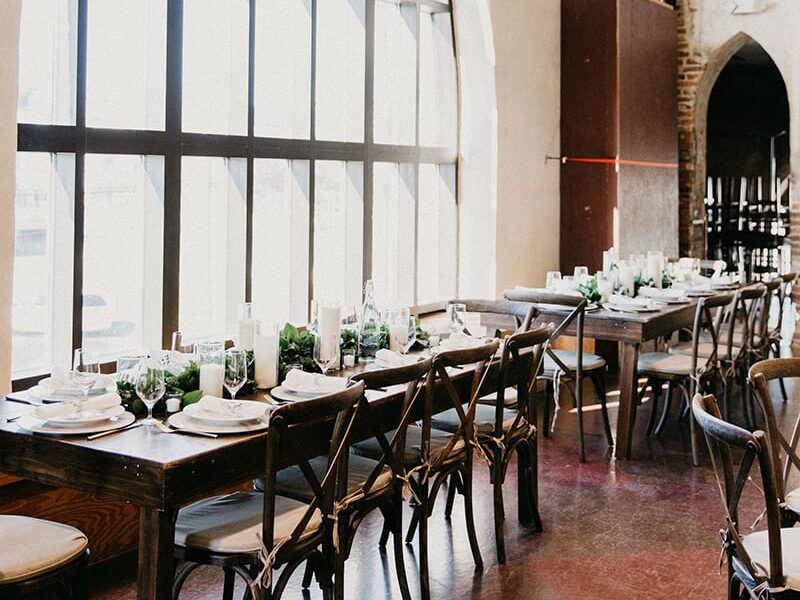 The indoor reception area with towering steeple stained glass with long tables adorned with china, candles, glass stemware and greenery.