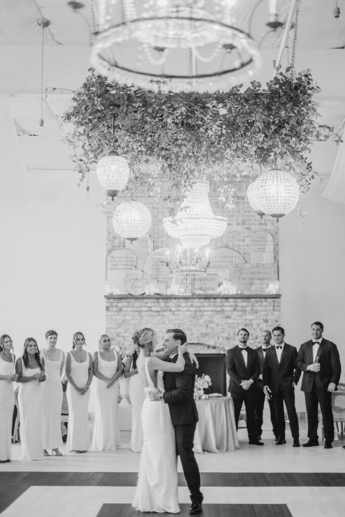 Couple dancing during their first dance under greenery, fireplace, and chandeliers in the background in Wilmington, NC.