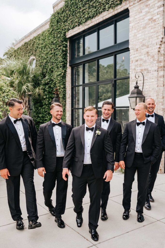 Groomsmen and groom having fun at his wedding with brick and greenery in the background in Wilmington.